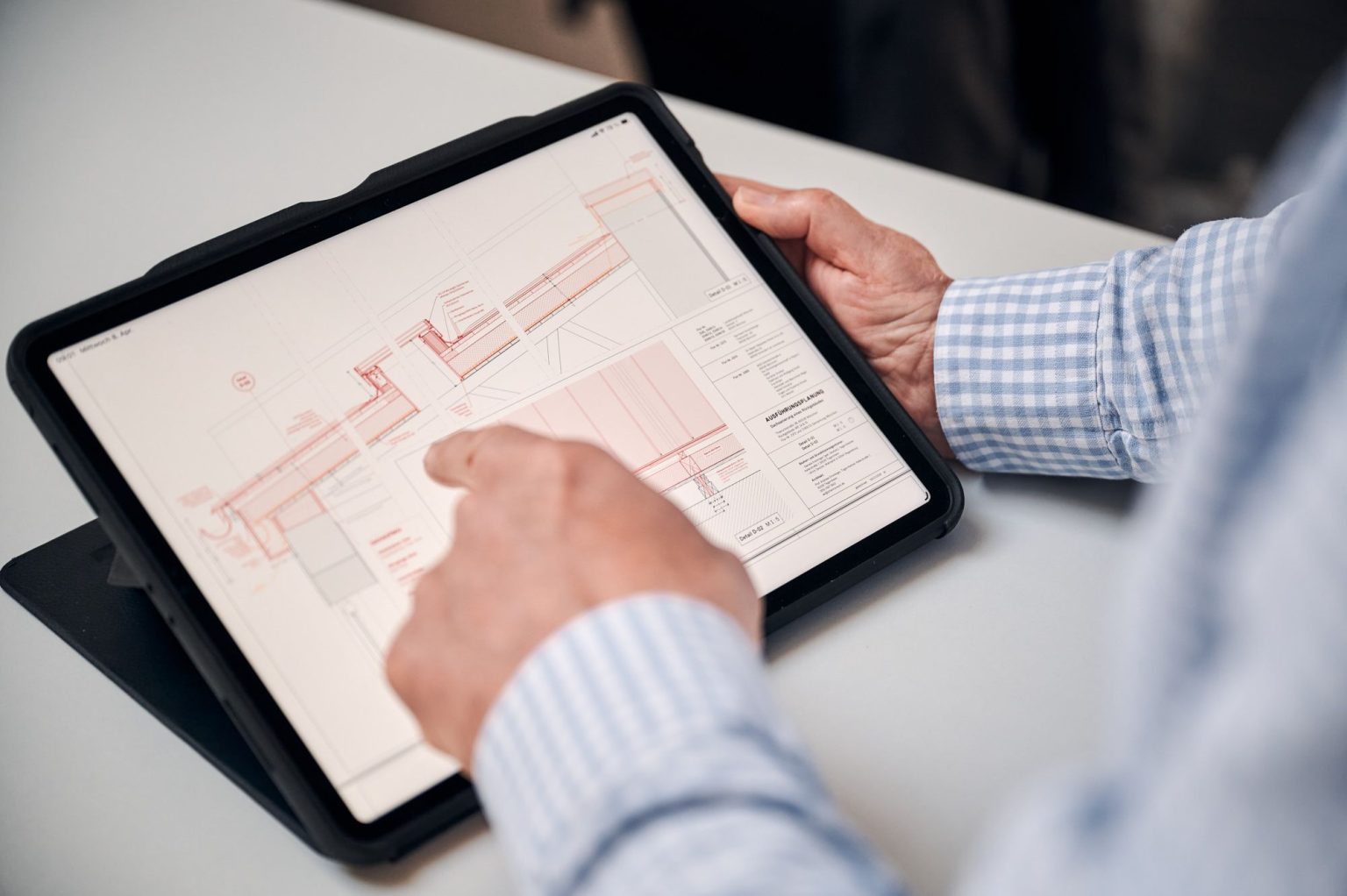 Person betrachtet digitale Baupläne auf einem Tablet, während sie mit dem Finger darauf zeigt.