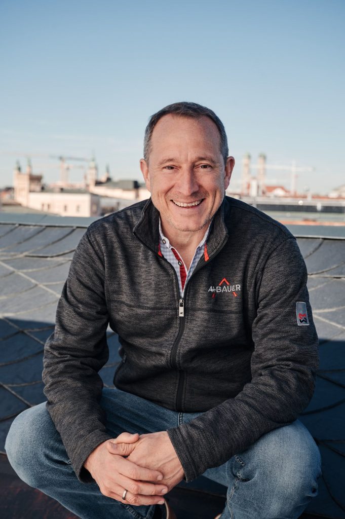 Betriebsleiter Michael Possnig sitzt auf einem Dach, trägt eine graue Jacke und hat eine Stadtlandschaft im Hintergrund.