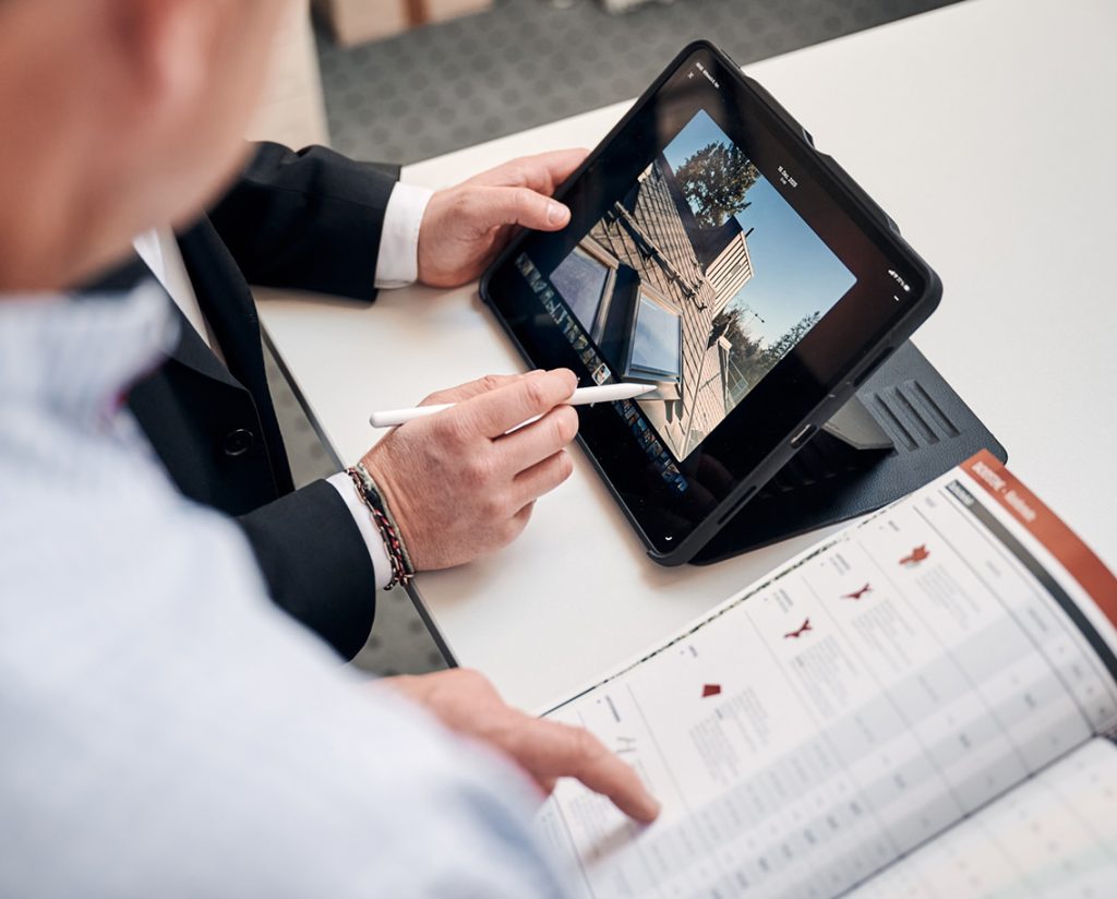 Mann mit Tablet und Stylus, der eine Baustelle plant, während er ein Handbuch auf dem Tisch studiert.