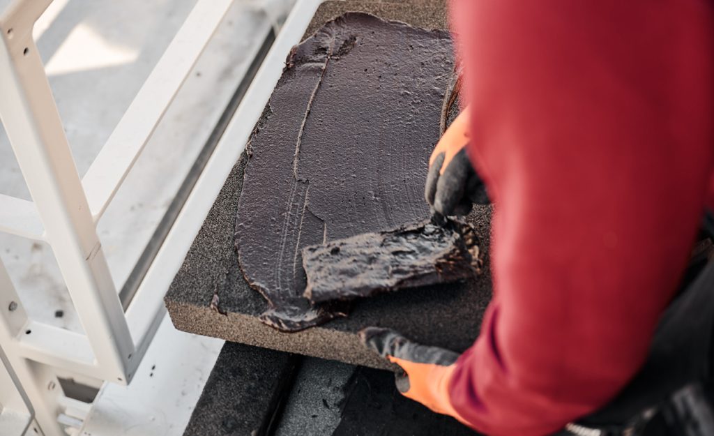 Arbeiter trägt schwarze Beschichtung auf eine Dämmplatte auf, um die Isolierung zu verbessern und Energieeffizienz zu steigern.