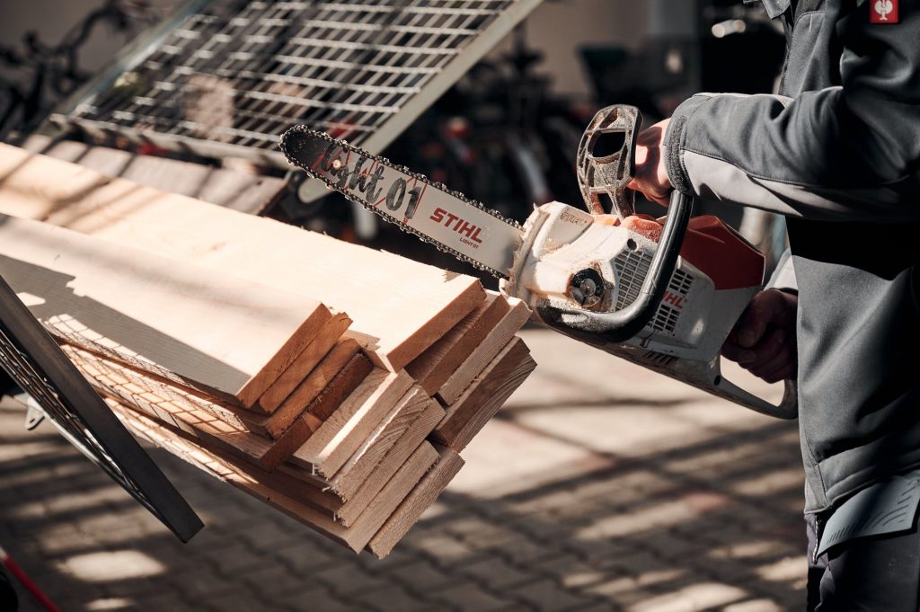 Eine Person hält eine STIHL Motorsäge über einem Stapel von Holzbretter. Bereit was zu sägen.