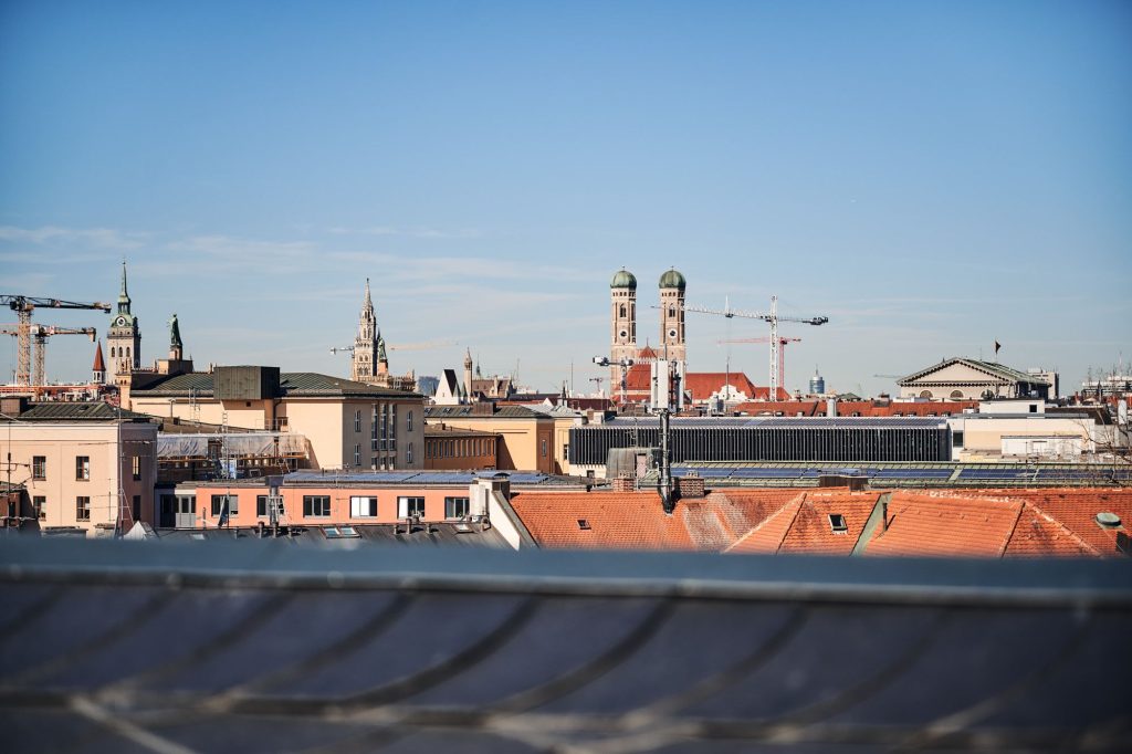 Blick auf die Dächer von München mit historischen Gebäuden und modernen Baustellen unter klarem Himmel.