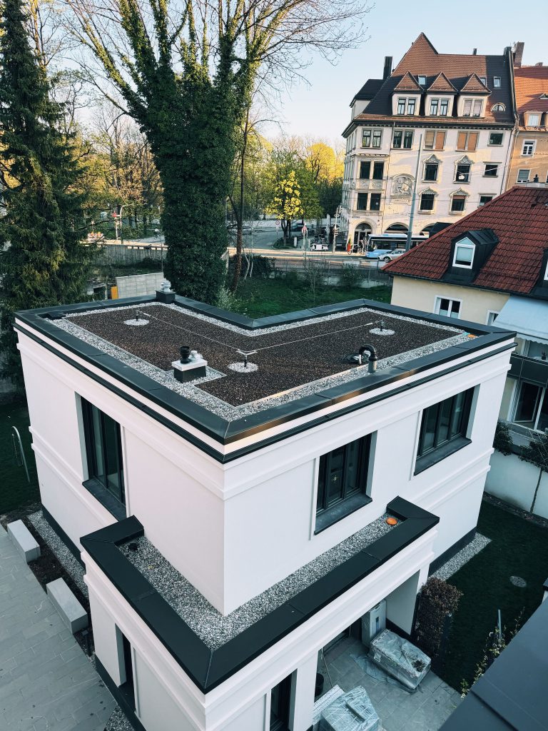 Moderne Architektur eines weißen Hauses mit begrüntem Dach, umgeben von Bäumen und historischen Gebäuden in der Stadt.