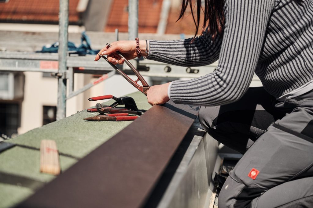 Handwerkerin auf dem Dach arbeitet mit Werkzeugen wie Zangen und Zirkeln.