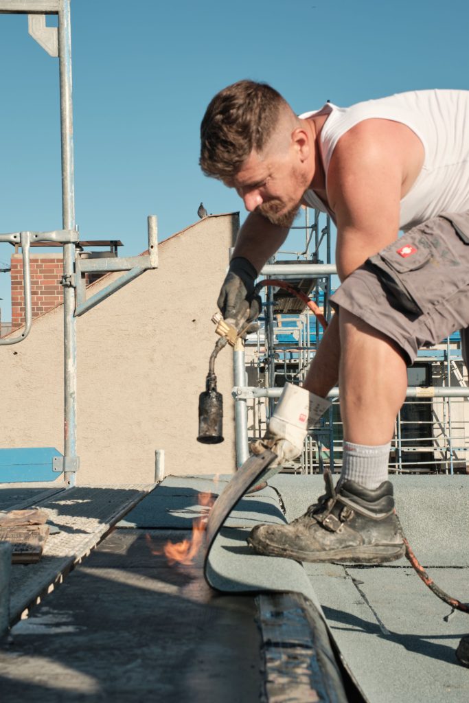 Handwerker auf dem Dach beim Verlegen von Dachmaterial mit einem Brenner, um die Materialien zu verbinden.