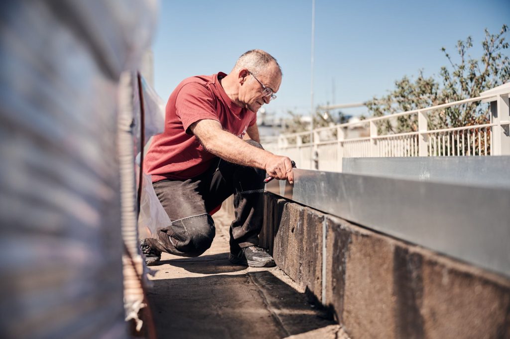Arbeiter überprüft präzise die Ausrichtung eines Metallstücks auf einer Baustelle im Freien.