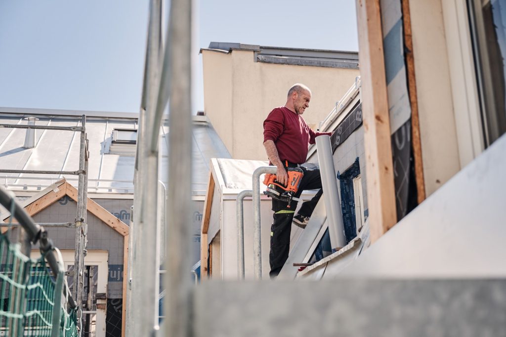 Handwerker auf einer Baustelle, der ein Werkzeug hält und an einem Gebäude arbeitet.