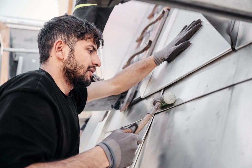 Handwerker bearbeitet Metallplatten mit einem Hammer, um eine präzise Anpassung während der Montage zu gewährleisten.