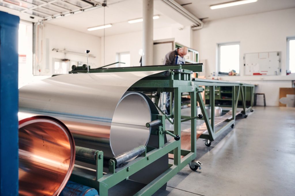 Eine Produktionsstätte mit einer Maschine zur Verarbeitung von Metallfolien, sichtbar Kupfer- und Aluminiumrollen.