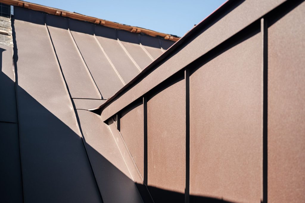Detailaufnahme eines modernen Daches mit brauner Metallverkleidung und klaren Linien im Sonnenlicht.