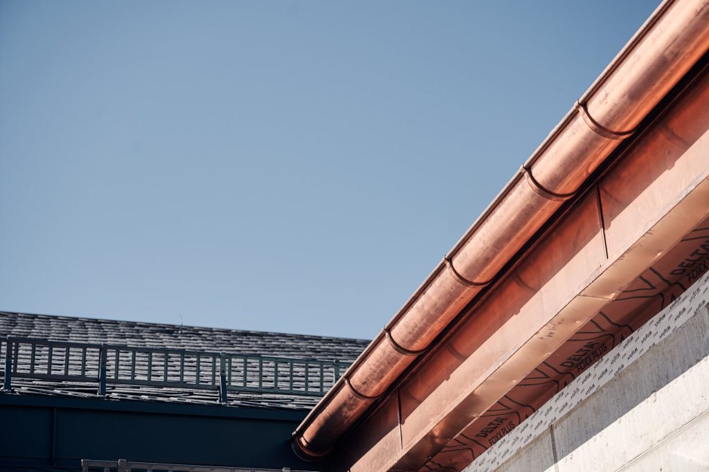 Dachdetails mit Kupferrinnen und Schiefer, vor blauem Himmel, zeigen moderne Architektur und Bauqualität.