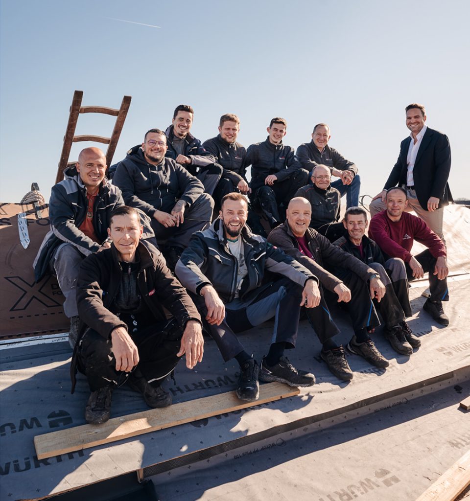 Gruppenfoto von Bauarbeitern auf einem Dach, die gemeinsam lächeln und in Arbeitskleidung posieren.