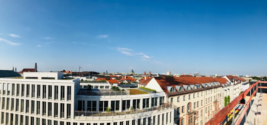 Panoramaansicht über Münchens Dächer, moderne Architektur und historische Gebäude unter blauem Himmel.