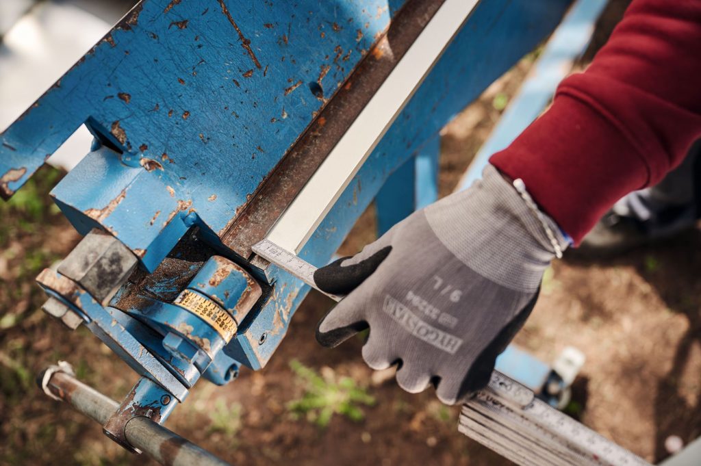 Hand mit Maßschieber an einer blauen Metallmaschine, die zur präzisen Bearbeitung von Materialien verwendet wird.