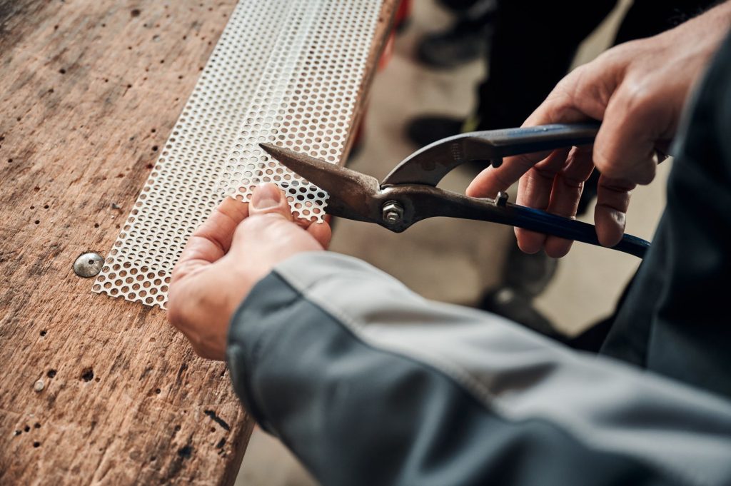 Handwerker schneidet in einer Werkstatt mit einer Zange ein Lochblech durch.