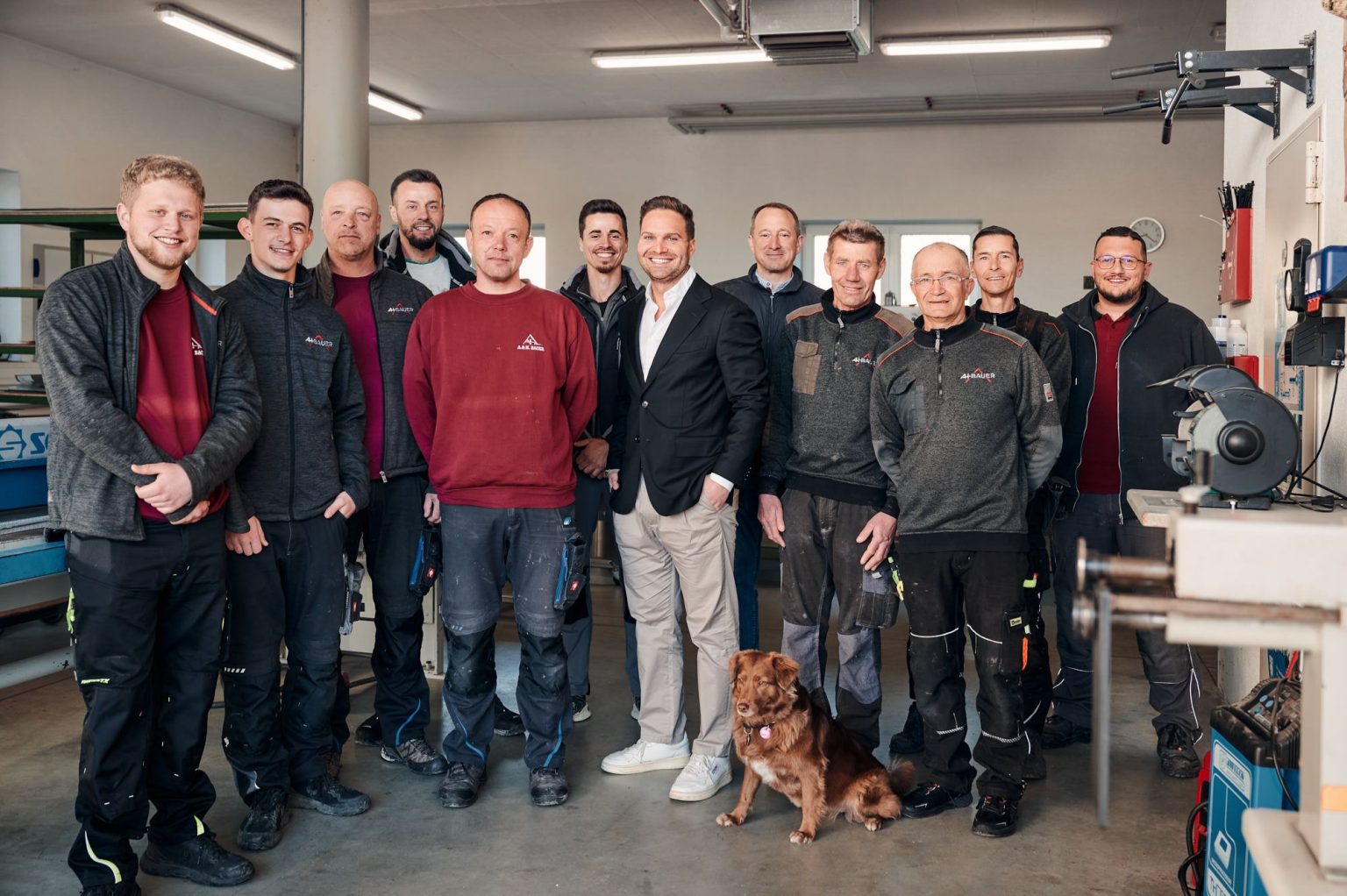 Teamfoto einer Handwerksgruppe in der Werkstatt, inklusive Mitarbeiter und Hund, lächelnd und zusammenstehend.