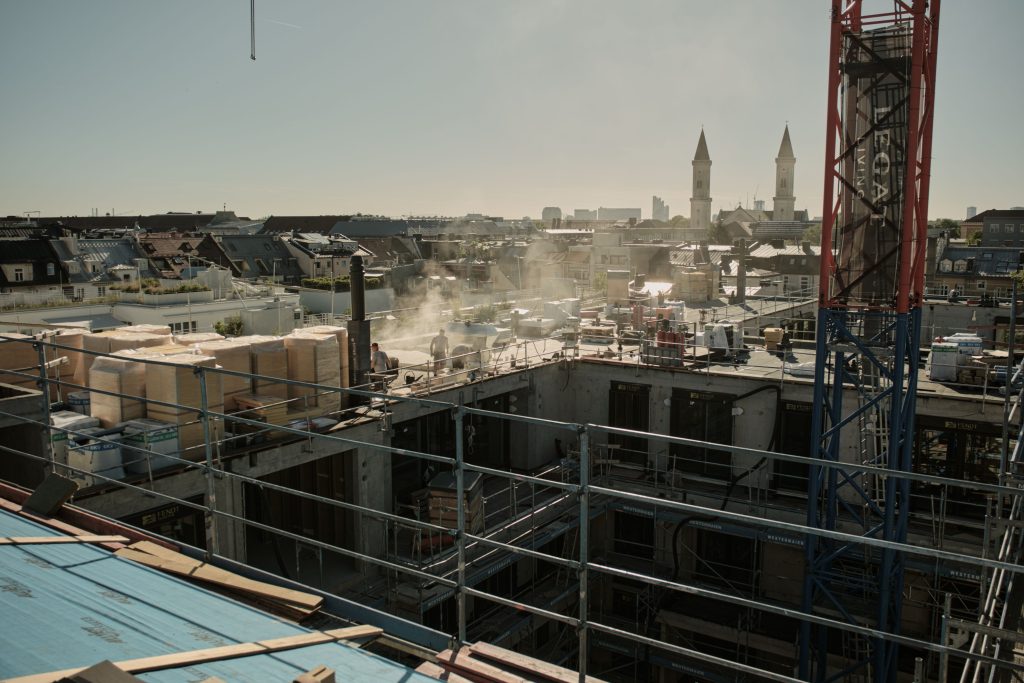 Bauarbeiter auf einer Baustelle mit Sicht auf die Stadt, umgeben von Baustellenmaterial und Gerüsten.